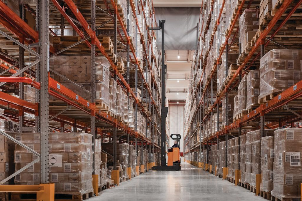 Orange Toyota Moving Mast Reach Truck putting products on shelf in warehouse