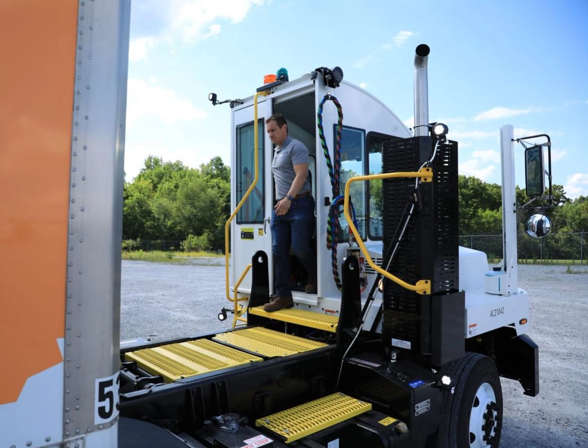 Man in gray shirt climbing yellow step ramp into white cab of utility truck with hydraulic lift equipment