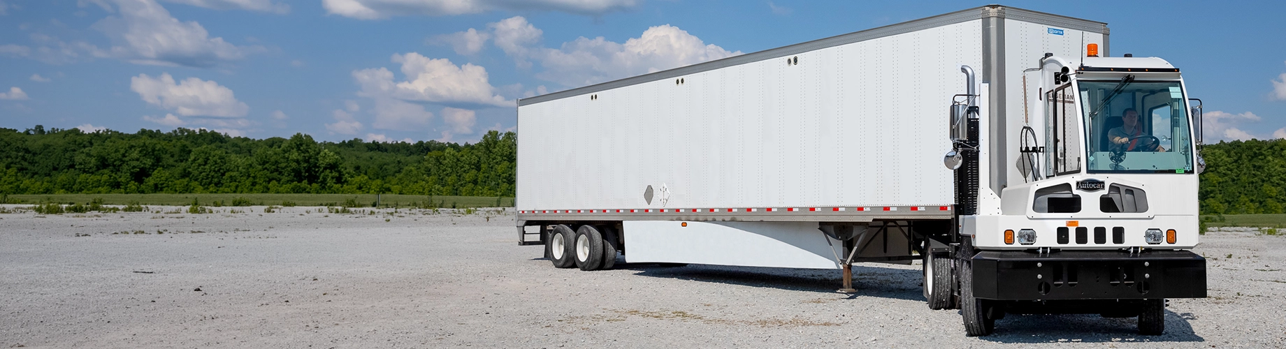 White refrigerated box truck with Thermo King unit parked on gravel with tree line and blue sky background